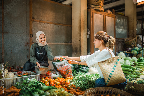 greengrocery seller helping customer picking vegetables from her stall in the farmer market