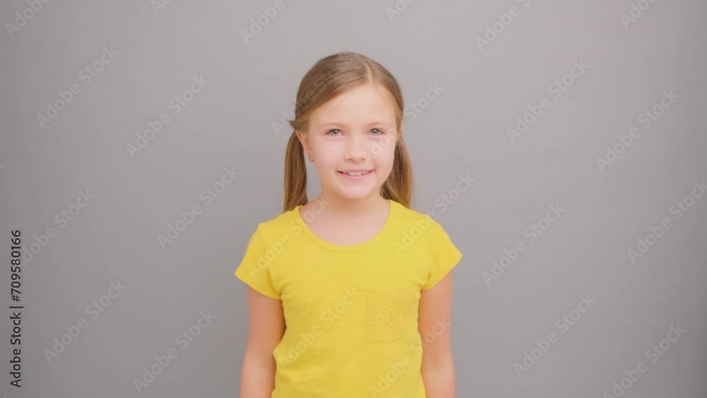 Happy little girl with pigtails wearing a yellow T-shirt on a gray background. Happy little girl with pigtails wearing a yellow T-shirt on a gray background.