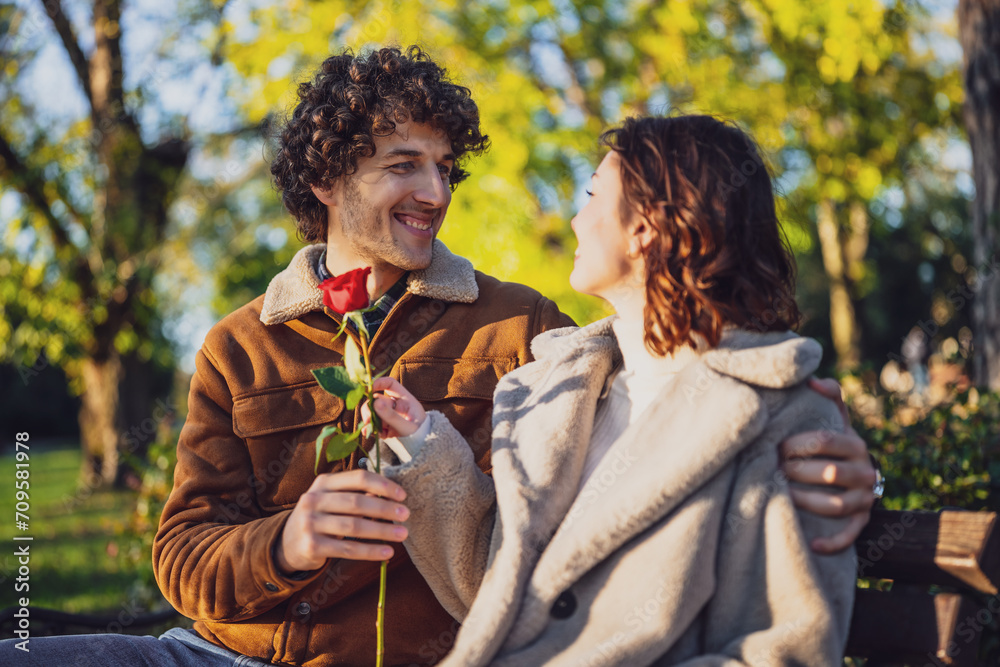 Fototapeta premium Portrait of happy loving couple in park. Man is giving rose to his woman.