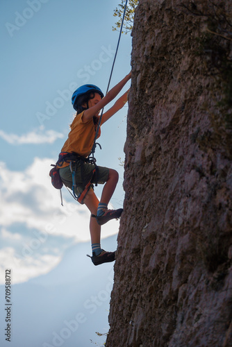 A determined and strong boy climber climbs a steep mountain wall. Extreme sports and rock climbing.