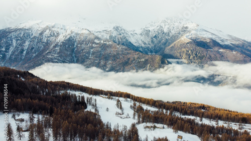 Aerial view of winter landscape with mountain peaks covered with snow, fluffy clouds and coniferous forest. Natural background.