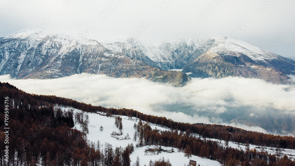 Aerial view of winter landscape with mountain peaks covered with snow, fluffy clouds and coniferous forest. Natural background.