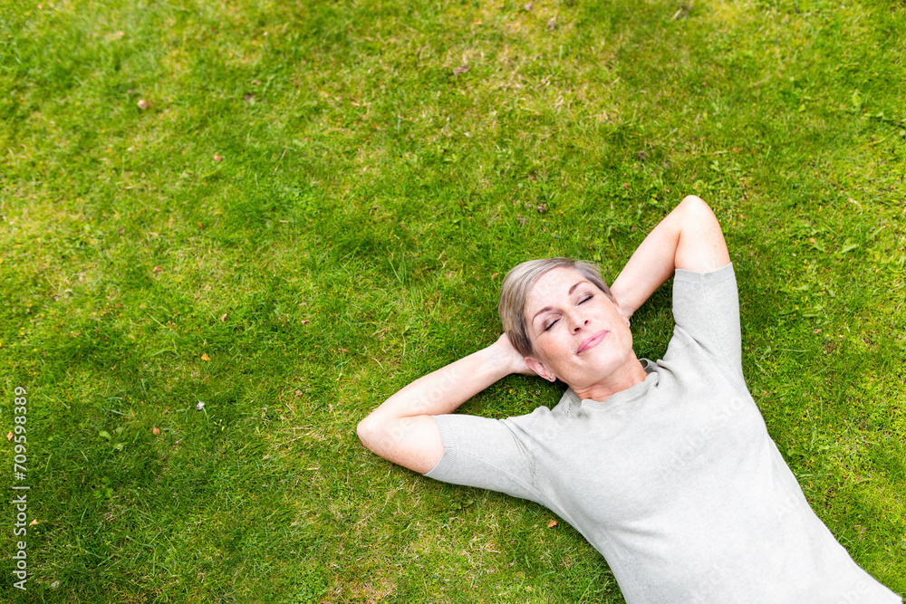 Carefree woman lying down with eyes closed on grass in garden Carefree woman lying down with eyes closed on grass in garden