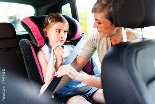 Mother helping daughter to fasten seat belt in car photo