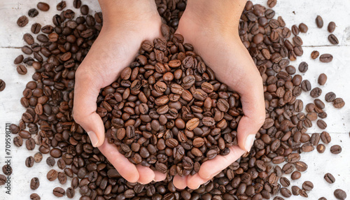 Two hands are full of roasted brown coffee beans
