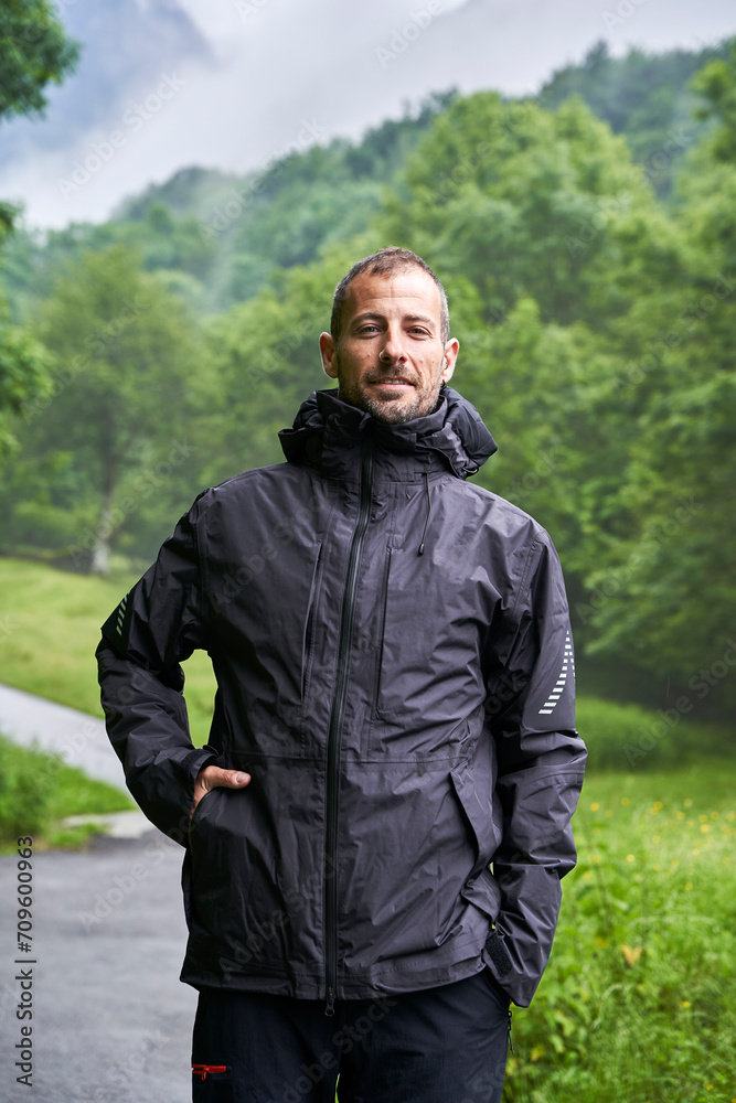 Smiling man wearing black jacket and standing in front of trees Smiling man wearing black jacket and standing in front of trees