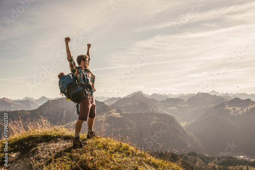 Young man standing on mountain top with arms raised in Tannheimer Tal, Tyrol, Austria photo