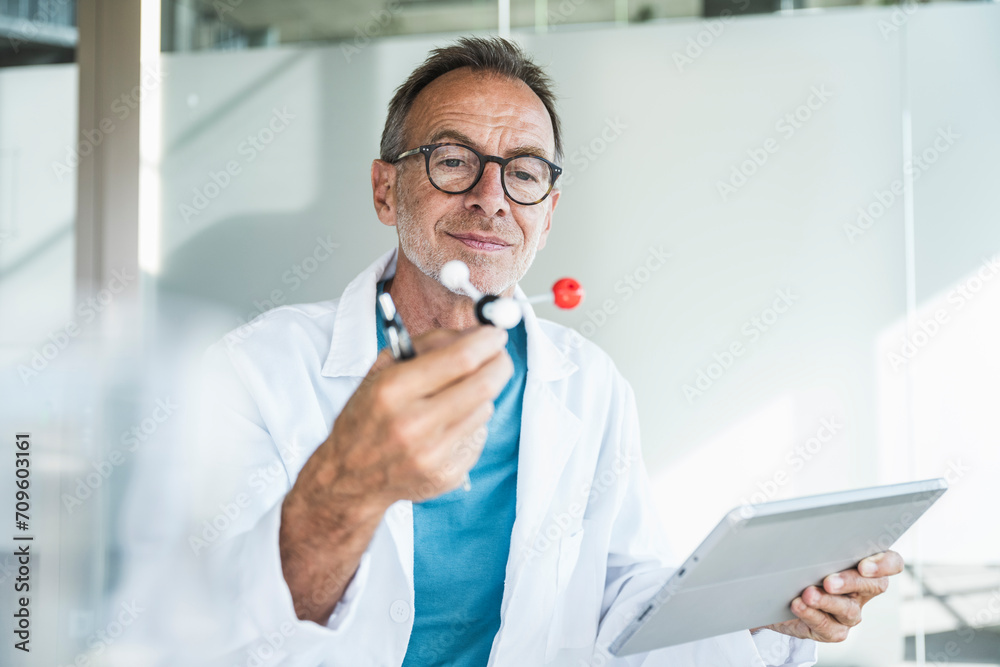 Smiling man in lab coat holding tablet PC and examining molecular structure Smiling man in lab coat holding tablet PC and examining molecular structure