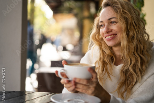 Smiling blonde woman in cafeteria. Beautiful lady relaxing in a coffee shop with cup of coffee. Close up face of girl drinking cappuccino.