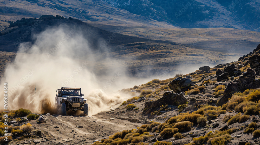 An off-road vehicle tackling rugged terrain in a mountainous landscape dust trailing behind.