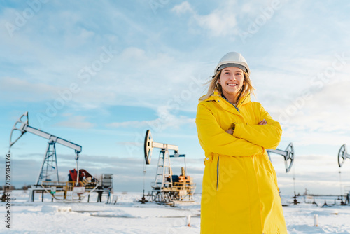 Smiling young engineer with arms crossed standing at oil production field in winter