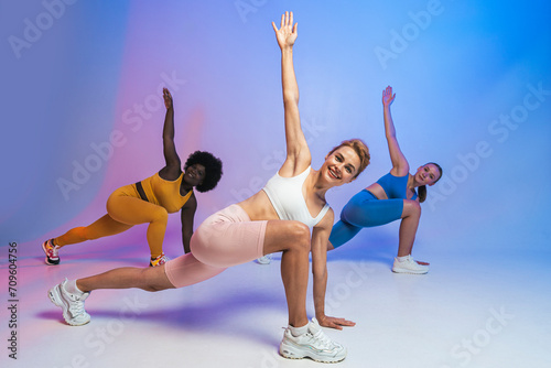 Happy multiracial female friends exercising together against colored background photo