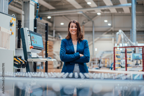 Smiling businesswoman with arms crossed by computer in industry photo