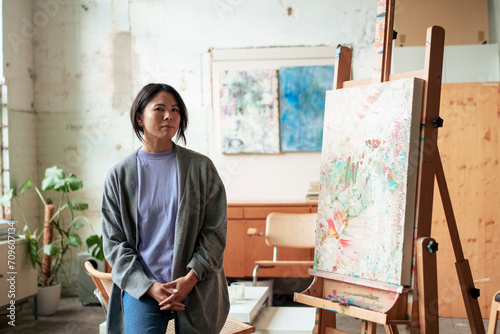 Confident artist standing by painting on easel in workshop photo