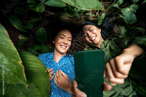 Smiling woman taking selfie on smart phone with friend lying amdist plants