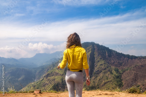 Rear view of lady enjoy at landscape Adam's peak mountain at tropical journey Sri Lanka, Ella, posing. From behind of adult woman in yellow jacket at landmark nature background. Copy ad text space