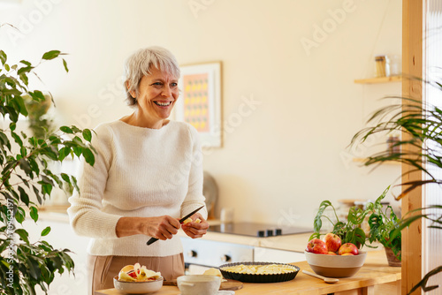 Happy mature woman cutting apple for pie in kitchen photo
