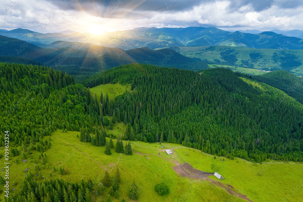 Scenic aerial view of the foggy Carpathian mountains, village and blue sky with sun and clouds in morning light, summer rural landscape