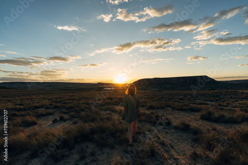 Woman walking amidst plants on desert landscape at sunset