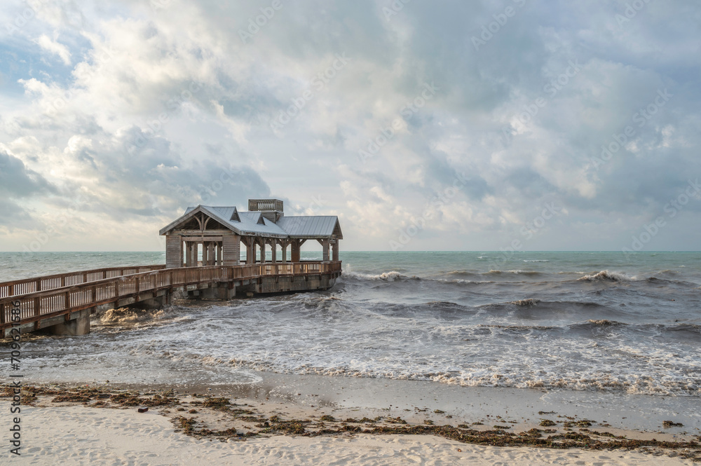 A wooden pier, with a covered portion at the end, reaching out into a choppy, rough sea