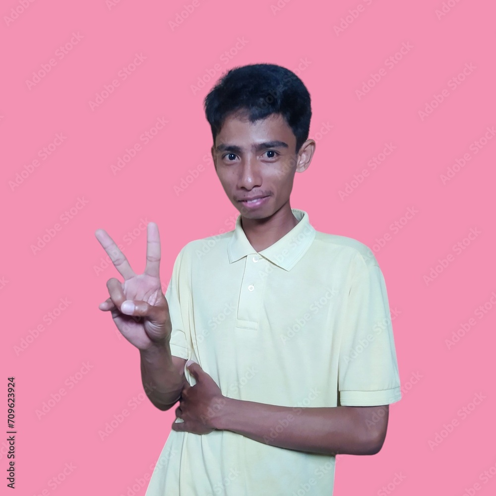 Young Asian man feeling happy and romantic forming heart gesture, wearing yellow t-shirt on pink background.