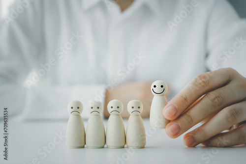 Hand choosing happy smiling wooden figure from unhappy sad. World mental health day, Think positive, Good emotion, positive attitude leadership, Excellent feedback and customer satisfaction concept.