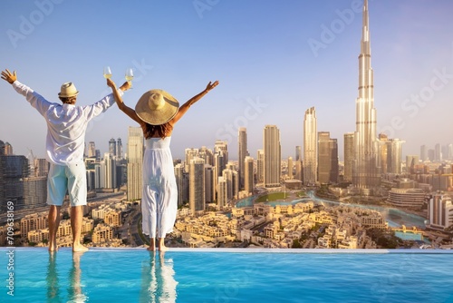A happy tourist couple on vacation time stands by the pool edge and enjoys the panoramic sunset view of the Dubai city skyline, UAE photo
