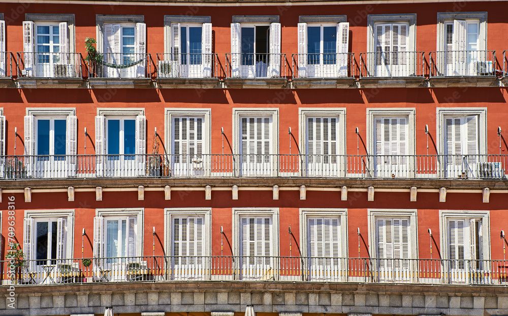 Front view of a colorful orange facade with white doors or jalousies. Balconies with white shutters or blinds on an orange exterior. Latin or Spanish architecture in Plaza Mayor - Madrid, Spain