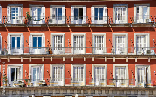 Front view of a colorful orange facade with white doors or jalousies. Balconies with white shutters or blinds on an orange exterior. Latin or Spanish architecture in Plaza Mayor - Madrid, Spain © Roberto