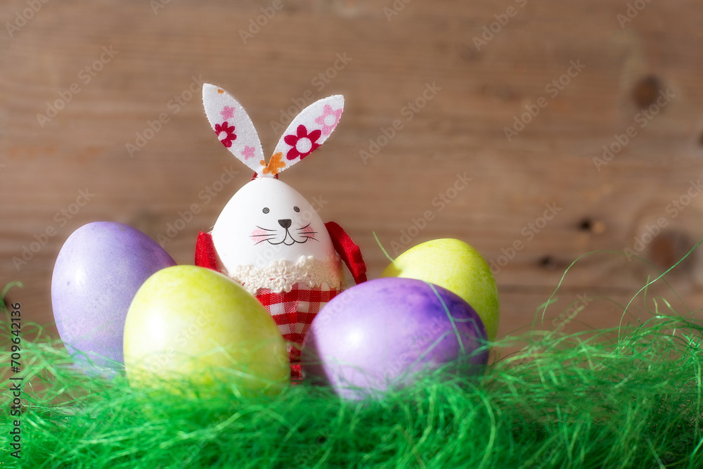 Colorful Easter eggs and bunny rabbit in green next decoration on wooden background