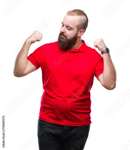 Young caucasian hipster man wearing red shirt over isolated background showing arms muscles smiling proud. Fitness concept.