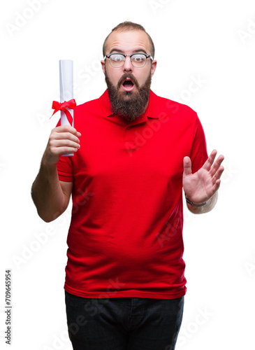 Young hipster man wearing glasses and holding degree over isolated background scared in shock with a surprise face, afraid and excited with fear expression