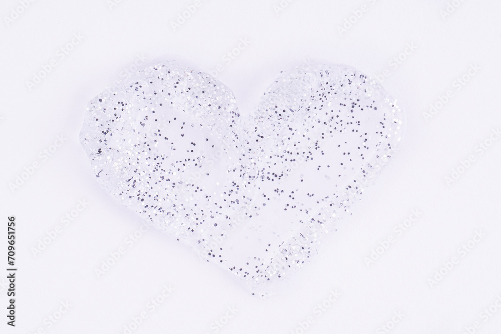 Cosmetic glittering gel in the shape of a heart. Transparent shimmer silver cosmetic sample texture on white background. Cosmetic shiny face serum, lotion, moisturizer,