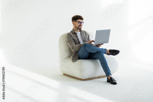 Portrait of attractive man sitting in chair using laptop calling contact over white background