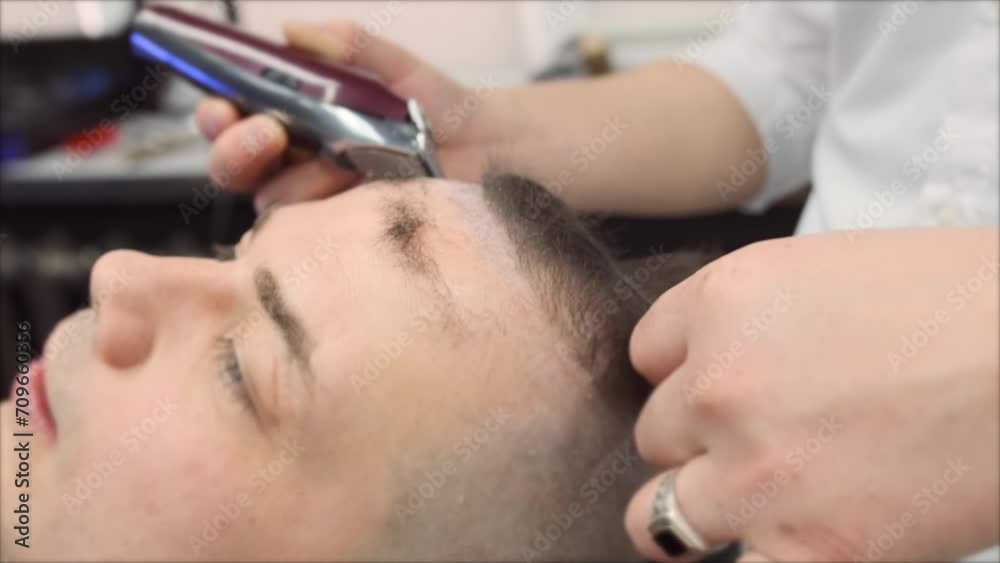 A barber stylist cuts hair from the forehead with a clipper for a male client. Close-up A barber stylist cuts hair from the forehead with a clipper for a male client. Close-up