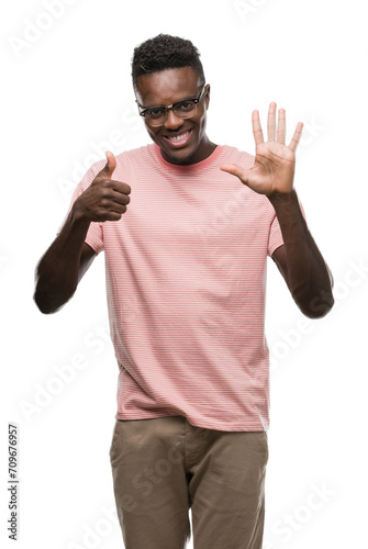 Young african american man wearing pink t-shirt showing and pointing up with fingers number six while smiling confident and happy. © Krakenimages.com