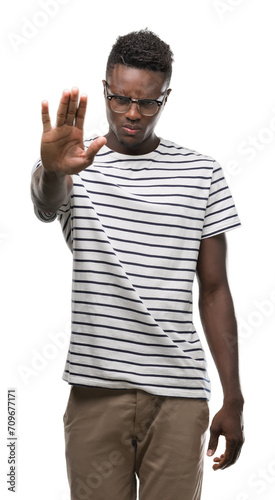 Young african american man wearing glasses and navy t-shirt doing stop sing with palm of the hand. Warning expression with negative and serious gesture on the face.