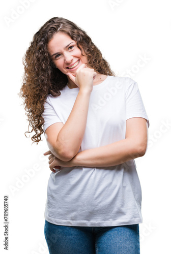 Beautiful brunette curly hair young girl wearing casual t-shirt over isolated background looking confident at the camera with smile with crossed arms and hand raised on chin. Thinking positive. © Krakenimages.com