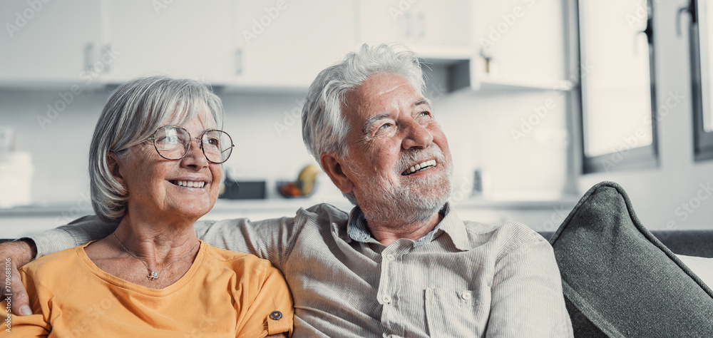 Obraz premium Dreamy middle aged senior loving retired family couple looking in distance, planning common future or recollecting memories, enjoying peaceful moment relaxing together on cozy sofa in living room.