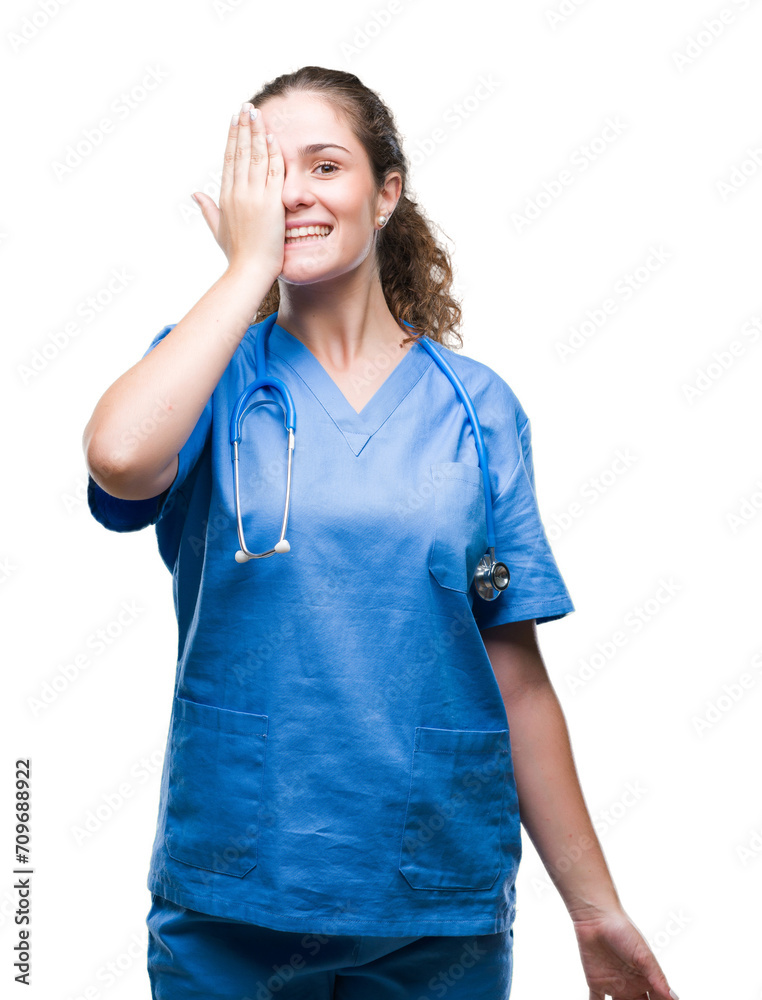 Young brunette doctor girl wearing nurse or surgeon uniform over isolated background covering one eye with hand with confident smile on face and surprise emotion. Young brunette doctor girl wearing nurse or surgeon uniform over isolated background covering one eye with hand with confident smile on face and surprise emotion.