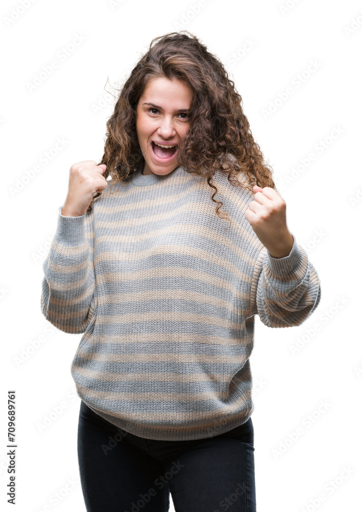Beautiful brunette curly hair young girl wearing winter sweater over isolated background very happy and excited doing winner gesture with arms raised, smiling and screaming for success Beautiful brunette curly hair young girl wearing winter sweater over isolated background very happy and excited doing winner gesture with arms raised, smiling and screaming for success