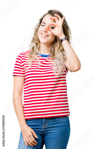 Beautiful young blonde woman over isolated background doing ok gesture with hand smiling, eye looking through fingers with happy face.