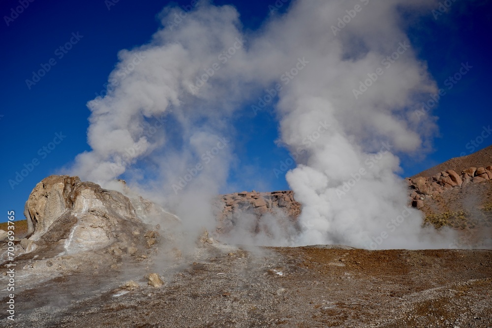 Steam rising from the ground with hills and blue skies behind, at Geysers Del Tatio, Antofagasta, Chile.