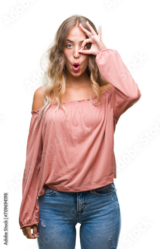 Beautiful young blonde woman over isolated background doing ok gesture shocked with surprised face, eye looking through fingers. Unbelieving expression.