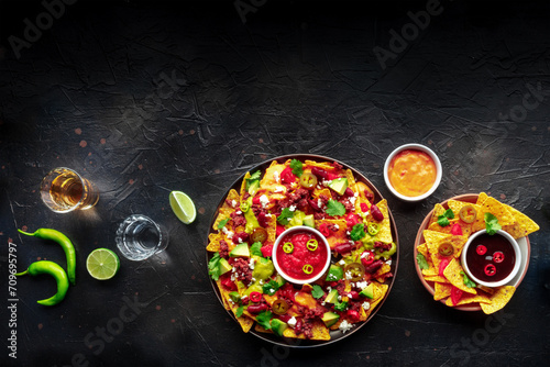 Loaded nachos. Mexican nacho chips with beef, overhead flat lay shot with guacamole sauce, cheese salsa, tequila drinks, limes, and chili peppers, with copy space