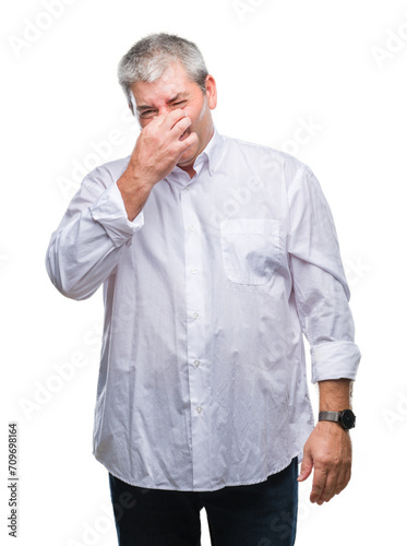 Handsome senior man over isolated background smelling something stinky and disgusting, intolerable smell, holding breath with fingers on nose. Bad smells concept. © Krakenimages.com