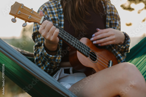 A young girl plays the ukulele while sitting in a hammock at sunset. Close-up. photo