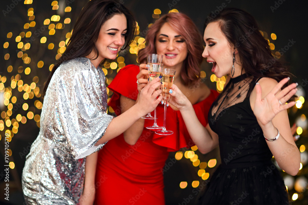 Smiling women in evening dresses with glasses of champagne over lights background