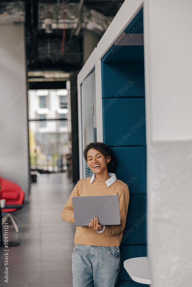 Pretty female freelancer working on laptop while standing on modern coworking background Pretty female freelancer working on laptop while standing on modern coworking background