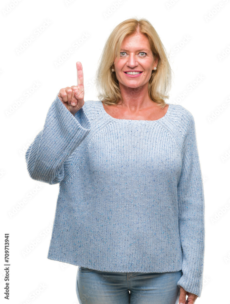 Middle age blonde woman wearing winter sweater over isolated background showing and pointing up with finger number one while smiling confident and happy. Middle age blonde woman wearing winter sweater over isolated background showing and pointing up with finger number one while smiling confident and happy.